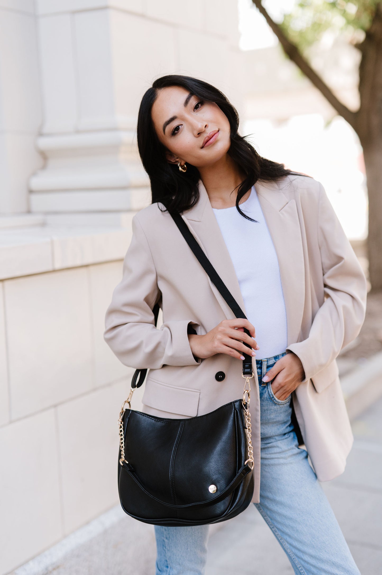 A woman standing in front of a white building wearing a black crossbody.
