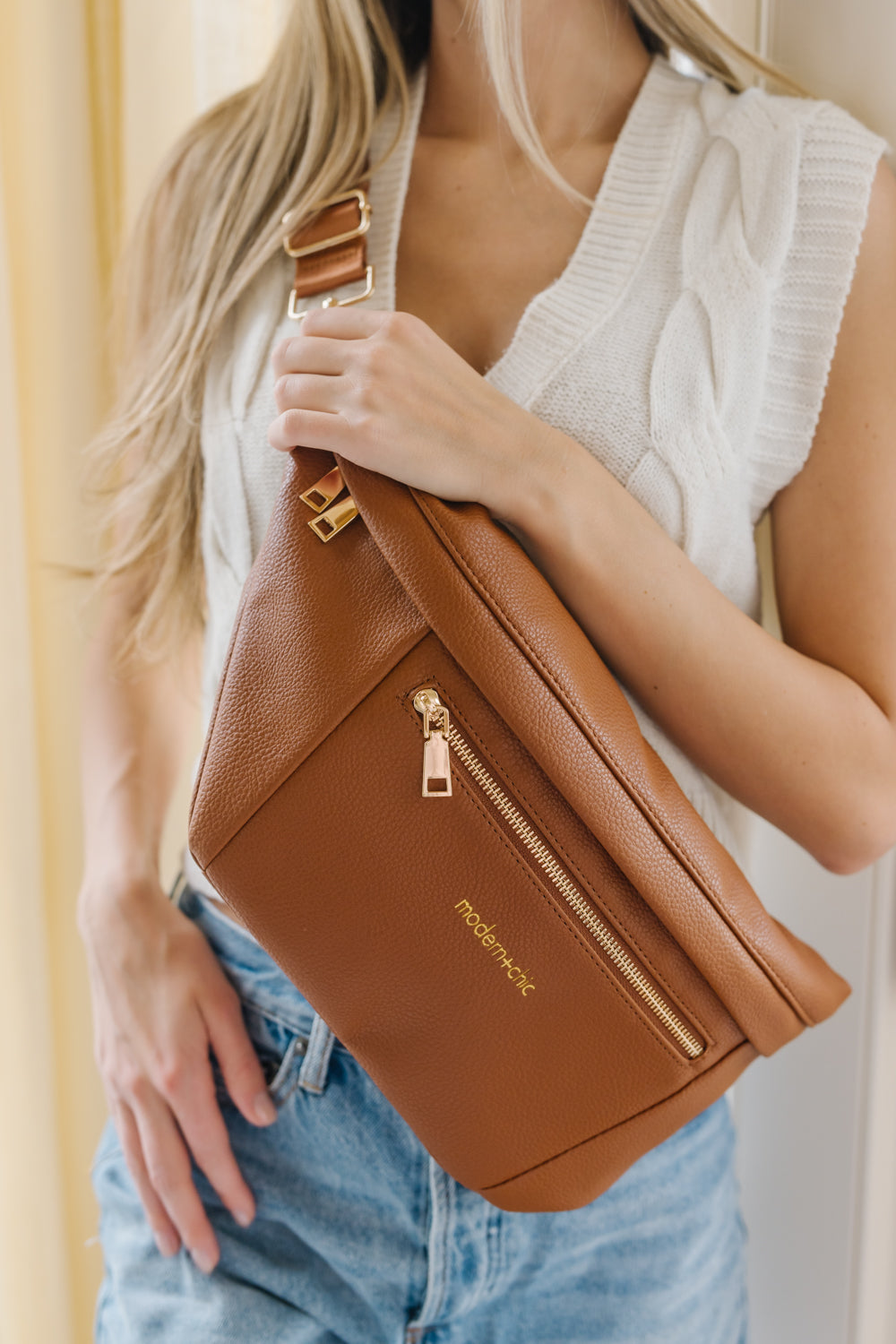 A woman wearing an oversized camel sling bag across her torso.