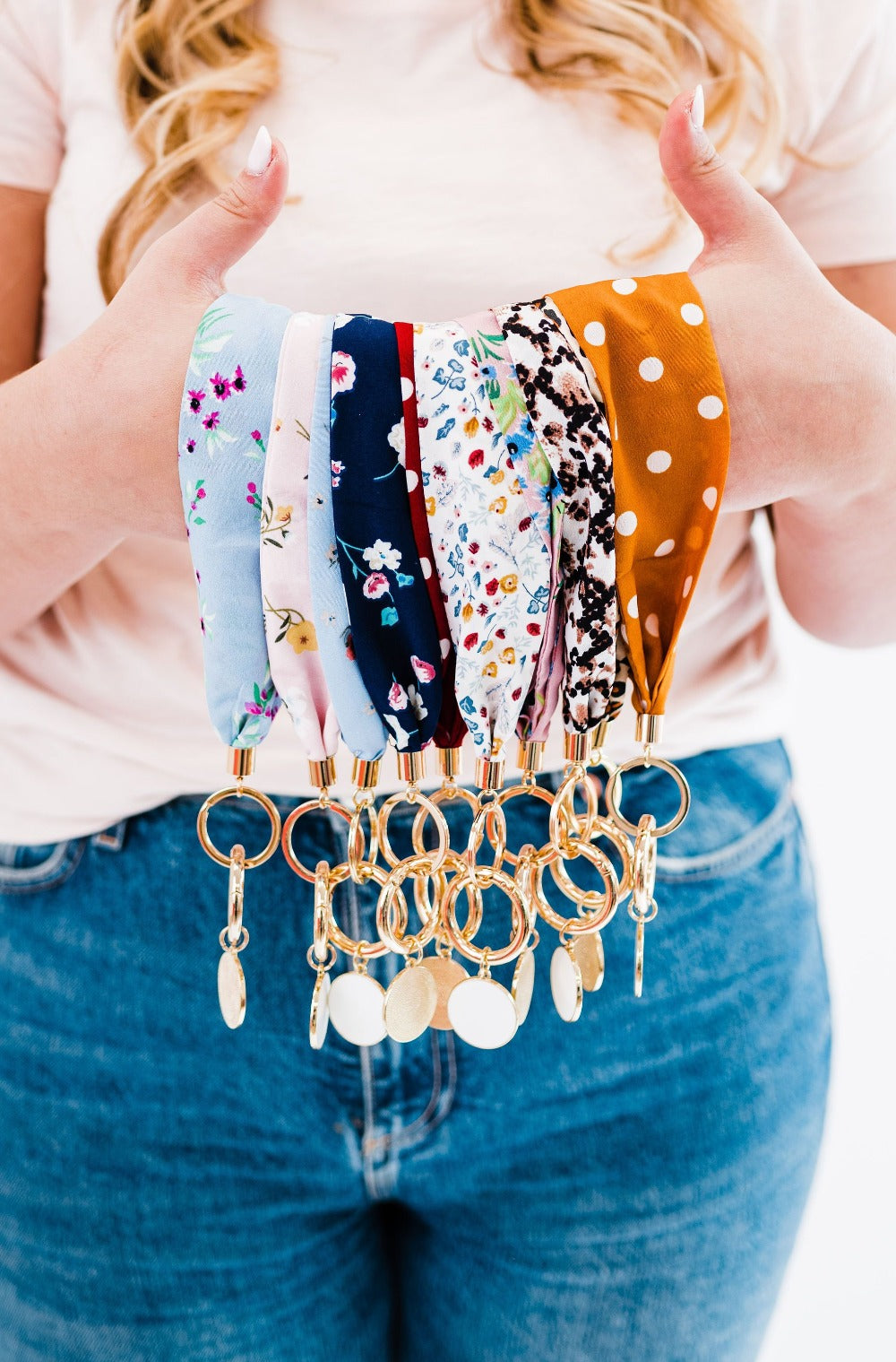 A person holding out Modern + Chic Luna Fabric Keychain Bracelets for Women- showcasing various patterns and colors such as animal print, floral, dots, and plain colors.