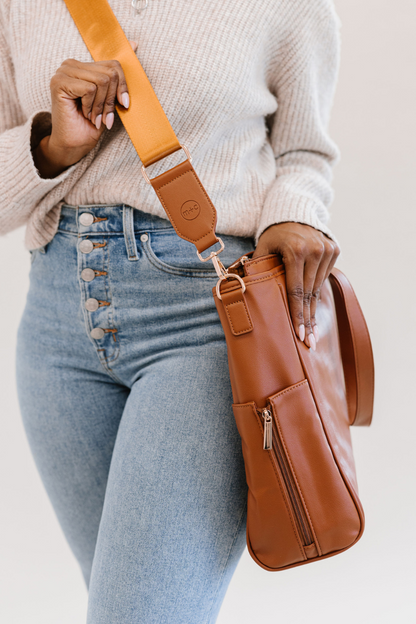 The strap on the brown tote has a stamped circular m+c logo on it. This tote also features side zipper pockets.