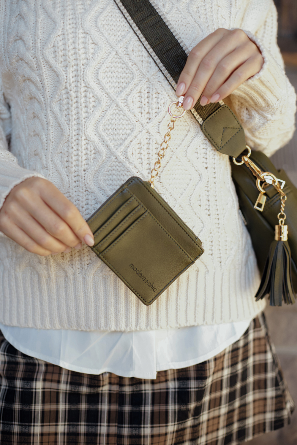 Person modeling an olive green Modern + Chic Alice Crossbody Vegan Leather bag holding a matching wallet with attached key leash. 