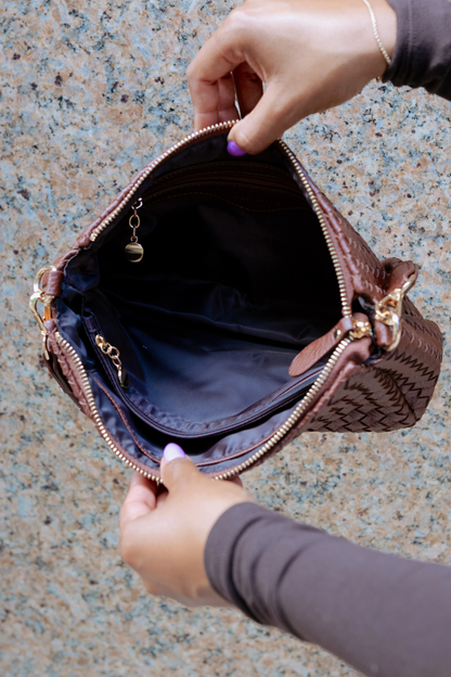 Brown textured Modern + Chic Elle Woven Crossbody Bag for Women with gold zipper being held open by a person on a speckled surface.