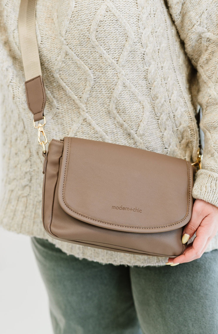 A woman wearing a taupe crossbody with the modern+chic logo on the front.