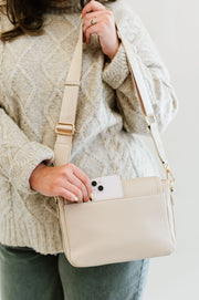 A woman putting her phone in the back magnetic slip pocket of the white crossbody.