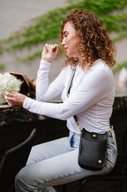 A woman wearing a small black crossbody bag with a woven strap