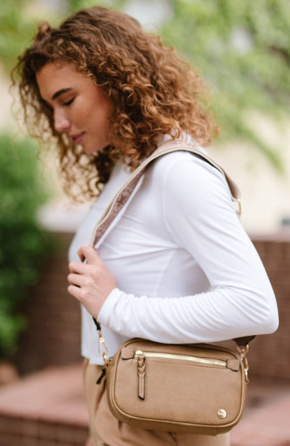 Woman wearing white shirt, tan pants and a Modern + Chic Gentry Vegan Leather Crossbody Bag in tan.