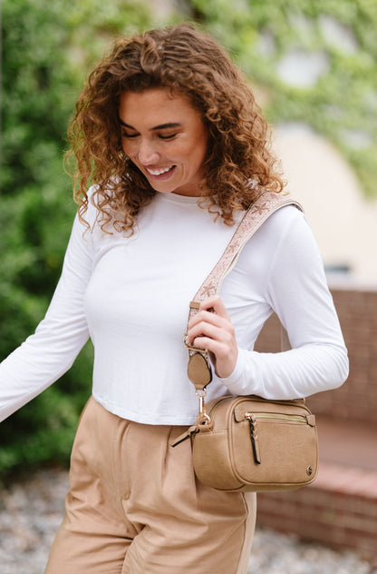 Woman wearing white shirt, tan pants and a Modern + Chic Gentry Vegan Leather Crossbody Bag in tan.