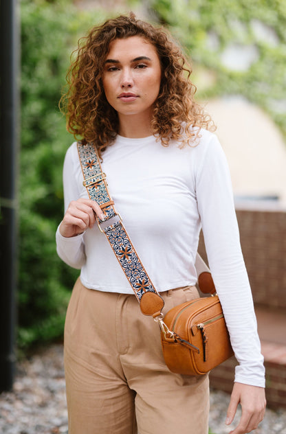 Woman wearing white shirt, tan pants and a Modern + Chic Gentry Vegan Leather Crossbody Bag in camel. 