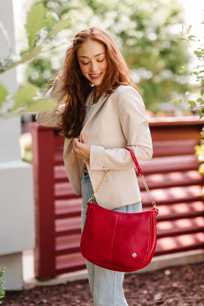 A woman wearing a red Modern + Chic Marissa Vegan Leather Saddle Crossbody Bag handbag over her arm. 