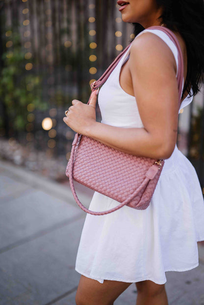 A woman wearing a pink Modern + Chic Elle Woven Crossbody Bag for Women over her shoulder outdoors.