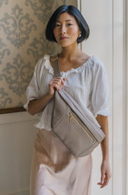 A woman wearing an oversized taupe sling bag across her torso.