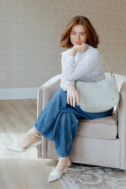 A woman posing with pebble or pale green Marissa Vegan Leather Saddle Crossbody Bag | Modern + Chic