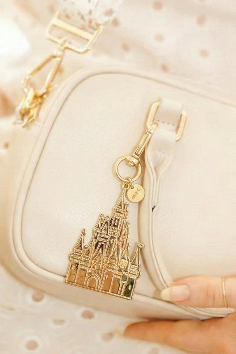 Modern + Chic Palace Charm – Gold castle-shaped keychain attached to a beige handbag.