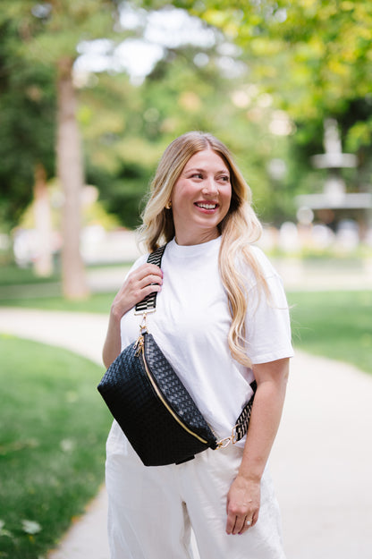 Woman wearing a white t-shirt and a black criss cross style Modern + Chic Rory Oversized Belt Bag for Women with a gold zipper and hardware crossbody.