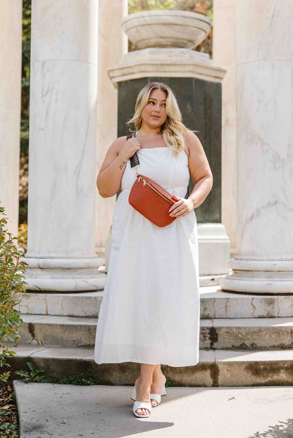 Woman wearing a white sundress and a copper criss cross style Modern + Chic Rory Oversized Belt Bag for Women with a gold zipper and hardware crossbody.