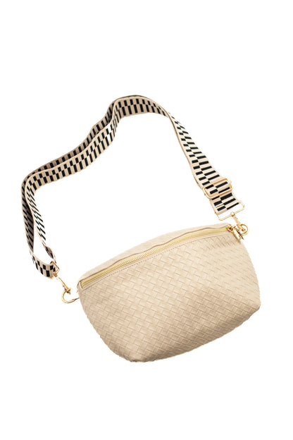 A cream criss cross style Modern + Chic Rory Oversized Belt Bag for Women with a gold zipper and hardware and a black and cream printed strap on a white background.